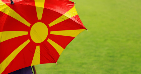Macedonia flag umbrella. Close up of printed umbrella over green grass lawn / field. Rainy weather forecast concept.	