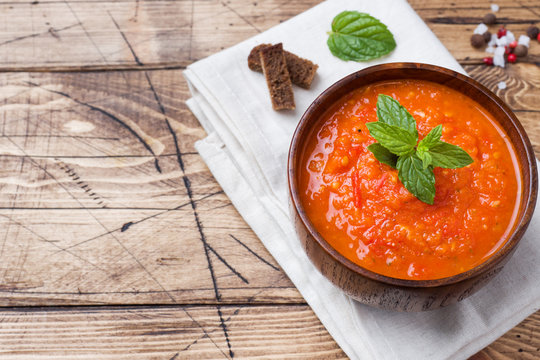 Tomato soup in a wooden bowl with pieces of toast on a rustic table.