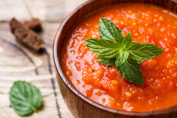 Tomato soup in a wooden bowl with pieces of toast on a rustic table.