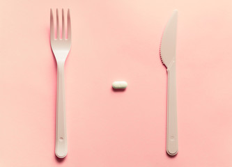 Fork, knife and pill on a pink background.