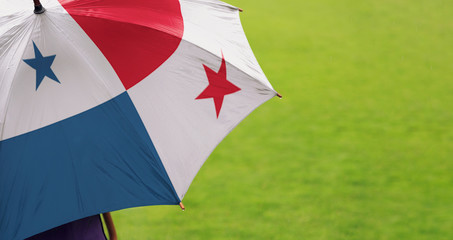 Panama flag umbrella. Close up of printed umbrella over green grass lawn / field. Rainy weather forecast concept.