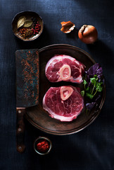 Osso buco raw steaks in a cast-iron pan, herbs and spices, top view