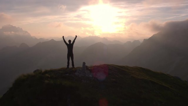 Aerial - Flyover silhouette of a man standing on top of the mountain