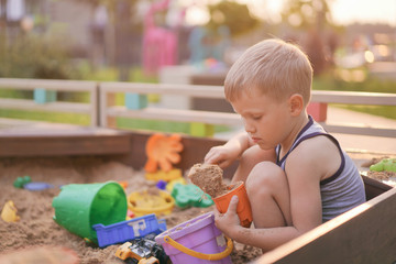 life of children in a modern city - little boy playing in the sandbox in the yard