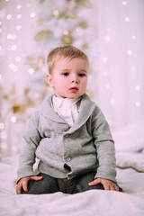 Naklejka premium Cheerful little baby boy playing near Christmas tree, gold and beige pastel c