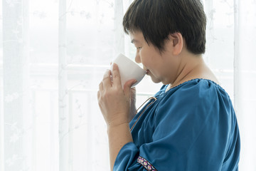 Asian Middle-aged woman drinking coffee in the morning next to the window