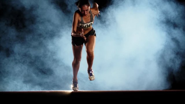 Runner speeding up. Asian female athlete blasting off in smoke on short track of stadium, training for competition 4k