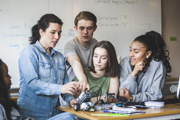 Teacher examining science project in classroom at high school