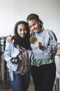 Portrait of female students holding gold medal and robot in classroom