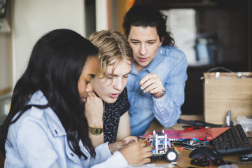 Teacher looking at students preparing toy car on desk in classroom