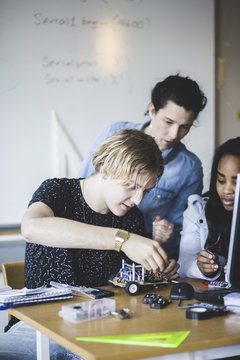 Mature female teacher looking at students preparing toy car on desk in classroom