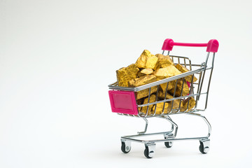 Pile of gold nuggets or gold ore in shopping cart or supermarket trolley on white background,...