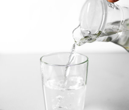 Hand pours water into a glass glass Cup from a glass jug. Close up. Isolated on white background