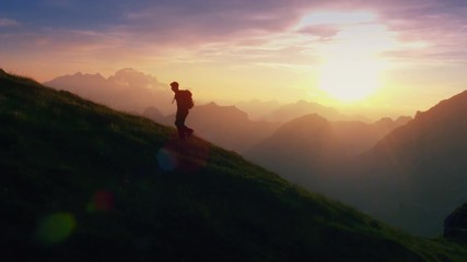 Aerial - Epic shot of a man hiking on the edge of the mountain as a silhouette in colorful sunset (edited) - Powered by Adobe