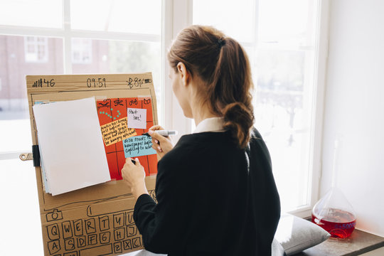 Rear view of businesswoman writing strategy on placard against window at creative office