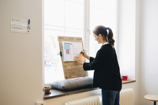 Confident businesswoman writing strategy on placard over window sill at creative office