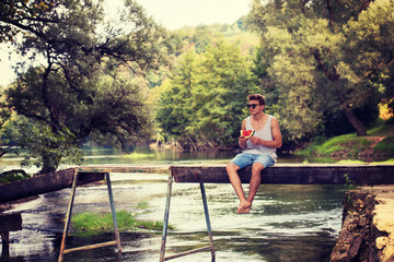man enjoying watermelon while sitting on the wooden bridge