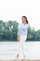 Full height portrait of beautiful brunette woman on the riverfront. Girl smiling looking