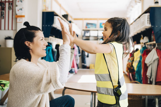 Side View Of Teacher And Girl Giving High Five In Cloakroom