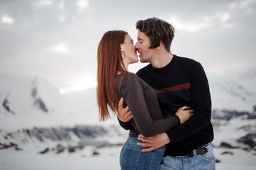 Young and beautiful lovers kissing on the background of snowy mountains