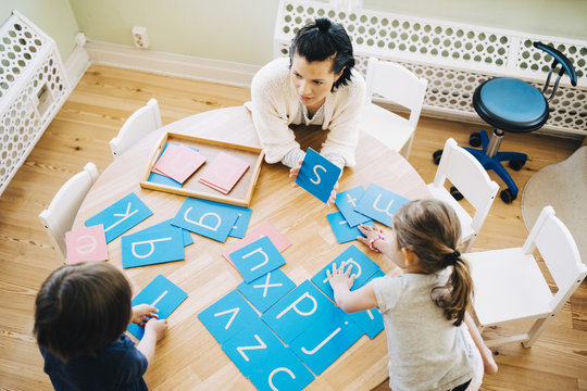 High angle view of confident female teacher showing letter S to students at table in classroom