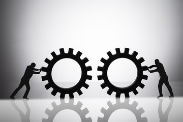 Silhouette Of Two Businesspeople Joining Gears
