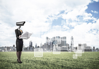 Camera headed woman standing on green grass against modern citys