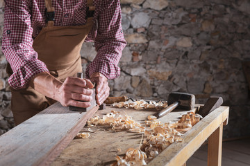 Man scraping plank while it sits on workbench