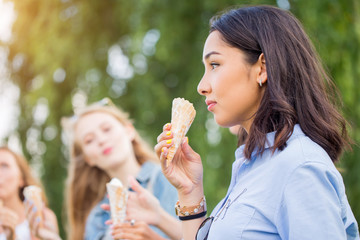 Obraz premium Three joyful young girlfriends on a promenade standing in a row smiling happily eat ice cream cones on summer vacation.