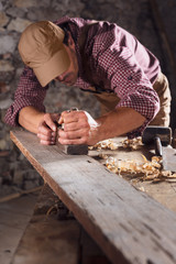 Carpenter smoothing out long wooden beam with tool