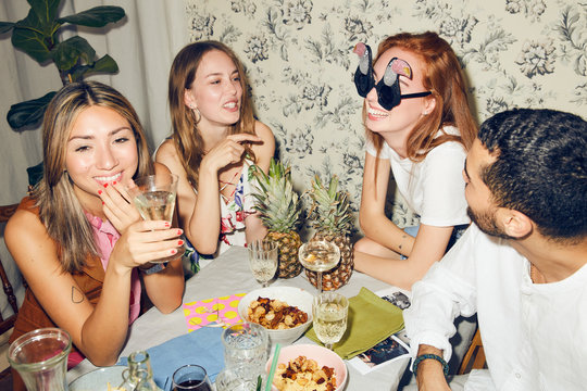 Young multi-ethnic friends celebrating at dining table during party in apartment