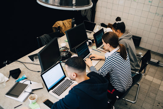 High angle view of young multi-ethnic hackers programming on laptops at desk in small office