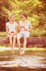 couple enjoying watermelon while sitting on the wooden bridge