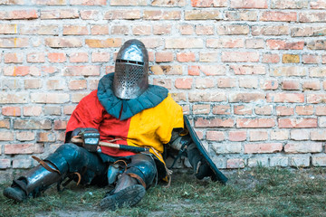 A medieval knight in armor sits by the wall.