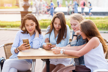 A group of young girls students sitting at a table in the Park and with a smile discussing something holding smartphones. chat, Internet, technology