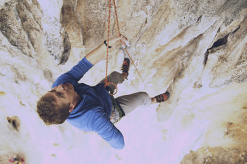 Young man looking up while climbing challenging route on cliff.
