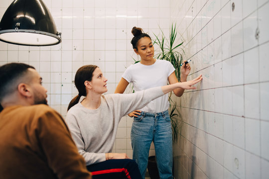 Young businesswoman brainstorming colleagues while writing strategy on tile wall at creative office