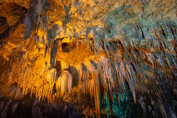 khao bin cave of Thailand, inside cave view of multiple small slender stalactites on the ceiling of a dark cave and a bright orange, Thailand.