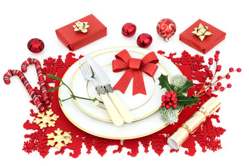 Christmas dinner table setting with plates, bauble decorations, gift boxes, cutlery, red bow and winter flora on red place mat on white background. Festive concept.
