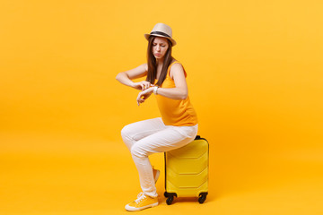 Traveler tourist woman in summer casual clothes, hat sit on suitcase isolated on yellow orange background. Female passenger traveling abroad to travel on weekends getaway. Air flight journey concept.