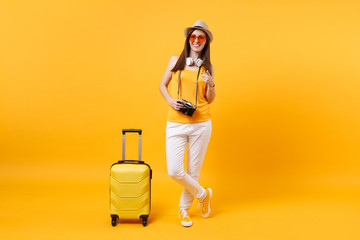 Traveler tourist woman in summer casual clothes, hat with headphones on neck isolated on yellow orange background. Passenger traveling abroad to travel on weekends getaway. Air flight journey concept.