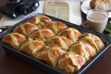 Hot cross buns with the cup of coffee, cinnamon sticks on the table