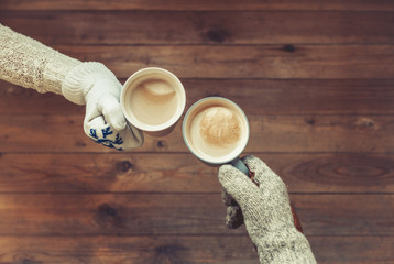 Male's and female's hands in the winter knitted mittens with an cup of coffee on the wooden table background. Winter concept