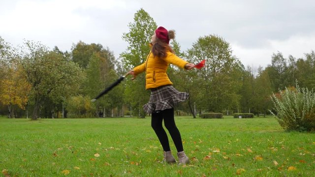 Happy woman dancing in park in yellow leaves with umbrella