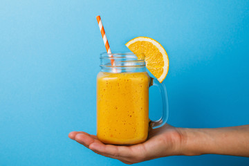 Freshly prepared smoothies from ripe orange in hand on blue background, close-up