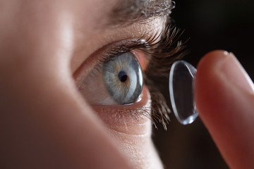 Close-up of a man putting contact lenses on blue eye. Concept of: healtcare, optic, hydration of the eye. - obrazy, fototapety, plakaty