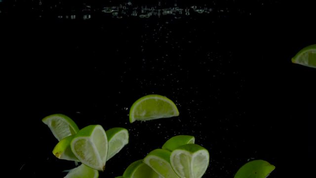 Lime pieces fall and float in water, black background. Slow motion