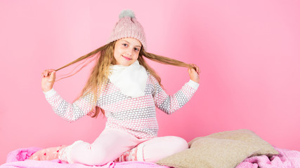 Obraz na płótnie Canvas Winter fashion accessory for kid. Winter accessory concept. Girl play long hair pink background. Kid smiling wear knitted accessory. Kid girl wear cute knitted fashionable hat and scarf accessory