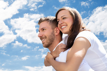 Obraz premium Happy Man Giving Piggyback To His Wife At Beach