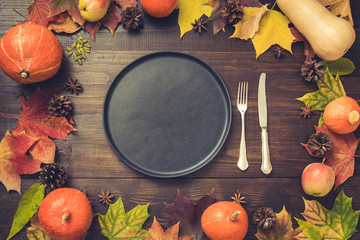 Autumn and Thanksgiving day table setting with fallen leaves, pumpkins, spices, empty black platter and vintage cutlery on brown wooden table. Top view, toned image. © svetlana_cherruty